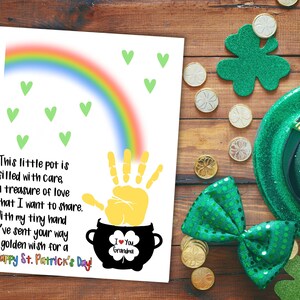May include: A white card with a rainbow, green hearts, and a yellow handprint. The handprint is inside a black pot with a shamrock and the text "I Love You Grandma". The card has the text "This little pot is filled with care, a treasure of love that I want to share. With my tiny hand I've sent your way a golden wish for a Happy St. Patrick's Day!"