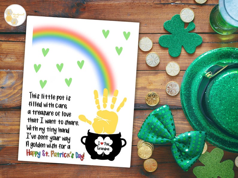 May include: A white card with a rainbow, green hearts, and a yellow handprint. The handprint is inside a black pot with a shamrock and the text "I Love You Grandma". The card has the text "This little pot is filled with care, a treasure of love that I want to share. With my tiny hand I've sent your way a golden wish for a Happy St. Patrick's Day!"
