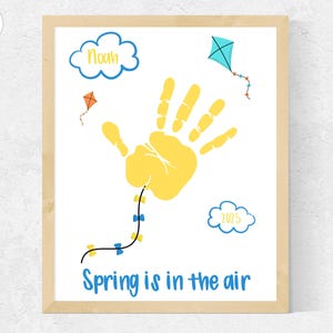 May include: A yellow handprint with blue bows hanging from it, a blue cloud with the text "2023" and another blue cloud with the text "Noah". The text "Spring is in the air" is at the bottom of the image.