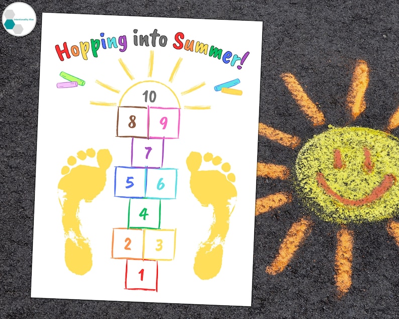 May include: A hopscotch game drawn on a white sheet of paper with yellow footprints and colorful squares numbered 1 to 10. The title "Hopping into Summer!" is written in rainbow colors. A yellow sun with a smiley face is drawn on a black asphalt surface.