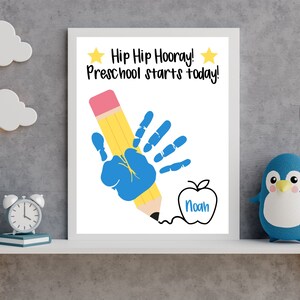 May include: A white printable sign with the text "Hip Hip Hooray! Preschool starts today!" and a blue handprint holding a yellow pencil. The pencil is drawing a red apple with the name "Noah" inside.