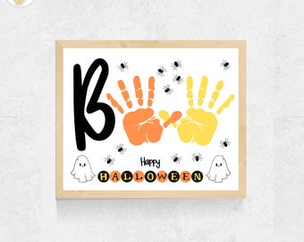 May include: A framed print featuring the word BOO in large black letters, two handprints in orange and yellow, and small black spiders. The text Happy HALLOWEEN is centered below with two white ghost illustrations on a white background.