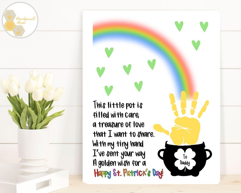 May include: A white card with a rainbow, green shamrocks, and a yellow handprint. The card has the text "This little pot is filled with care, a treasure of love that I want to share. With my tiny hand I've sent your way A golden wish for a Happy St. Patrick's Day!" and "To Daddy".