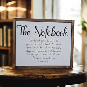 May include: A wooden framed sign with the words "The Notebook" in a stylish script. The sign displays a romantic quote about love, suitable for home decoration. The background is white, and the frame is dark brown.