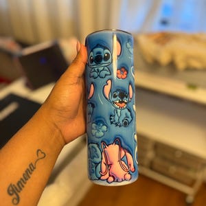 Puede incluir: Un vaso de acero inoxidable azul con un dise&ntilde;o colorido que presenta a Stitch de Lilo & Stitch. El dise&ntilde;o incluye a Stitch en varias poses, flores rosas y un fondo azul.