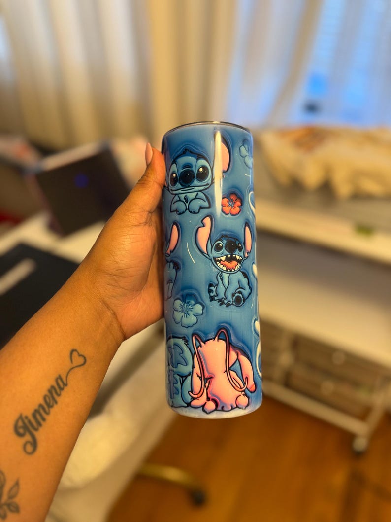 Puede incluir: Un vaso de acero inoxidable azul con un dise&ntilde;o colorido que presenta a Stitch de Lilo & Stitch. El dise&ntilde;o incluye a Stitch en varias poses, flores rosas y un fondo azul.