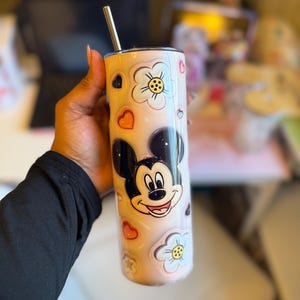 May include: A stainless steel tumbler with a pink and white floral design featuring Mickey Mouse. The tumbler has a straw and is perfect for holding hot or cold beverages.