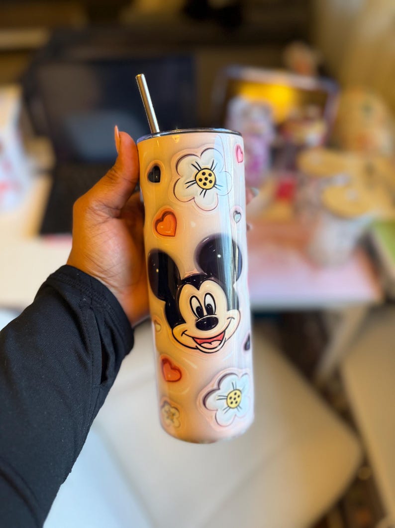 May include: A stainless steel tumbler with a pink and white floral design featuring Mickey Mouse. The tumbler has a straw and is perfect for holding hot or cold beverages.