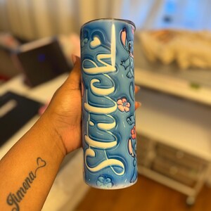 Puede incluir: Un vaso de acero inoxidable azul y blanco con un personaje de dibujos animados y la palabra "Stitch" en letras blancas.