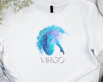 Puede incluir: Una camiseta blanca de manga corta con un gráfico central de una figura estilizada con cabello fluido azul y morado, rodeada de pequeños puntos blancos como estrellas. Debajo del gráfico, la palabra VIRGO está impresa en letra oscura.
