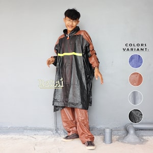 Può includere: Una persona indossa un impermeabile nero con una striscia gialla e pantaloni marroni. L'impermeabile ha un cappuccio ed è realizzato in materiale impermeabile. La persona è in piedi davanti a un muro grigio. L'immagine mostra anche una selezione di colori per l'impermeabile, tra cui blu, marrone, grigio e nero.