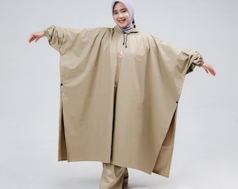 Op de afbeelding: Een beige regenjas met capuchon en een trekkoord. De regenjas heeft lange mouwen en een losse pasvorm. Het model draagt de regenjas met een lichtgrijze hijab.