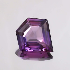 May include: A purple gemstone with a faceted, square-shaped cut. The gemstone has a slight gradient of colour from a darker purple to a lighter purple.