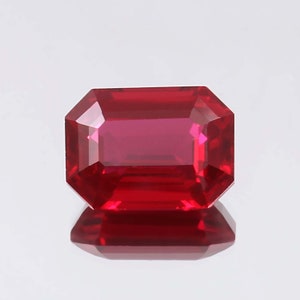 May include: A rectangular-cut ruby gemstone, displaying a rich, deep red hue. The facets of the stone are precisely cut to enhance light reflection. The gemstone is presented against a white backdrop, highlighting its clarity and brilliance. The gem is a beautiful example of its type.