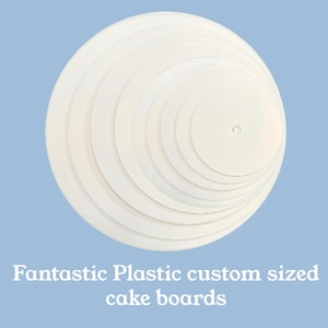 May include: A set of white circular cake boards arranged in a nested, concentric pattern from largest to smallest. The smallest board features a small center hole. The text "Fantastic Plastic custom sized cake boards" is printed below the boards.