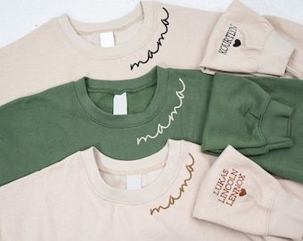 Puede incluir: Tres sudaderas con texto bordado. Una es beige con texto marrón que dice "mama" y "LUKAS LINCOLN LENNOX" con un corazón. Otra es verde con texto blanco que dice "mama". La última es beige con texto negro que dice "mama" y "KOURTLIN" con un corazón.