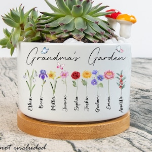 May include: White ceramic planter with the text "Grandma's Garden" and a floral design featuring different flowers and butterflies. The planter has a wooden base and is filled with succulents and a small mushroom figurine.
