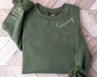 May include: A dark green sweatshirt with the word "love" embroidered on the front in a gold script font. The left sleeve has the names "Liam", "Ethan", "Sophia" embroidered in gold with a small heart symbol.