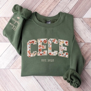 May include: A green sweatshirt with a floral print design that spells out "CECE" and the text "EST. 2025" below. The sweatshirt has a heart and the text "Elmore" on the sleeve.