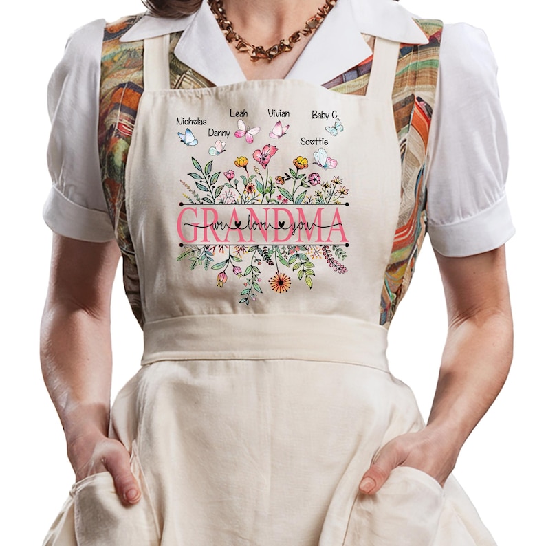 May include: A white apron with a floral design and the text "We love you Grandma" in pink. The apron has pockets on the sides and butterflies with names on them.