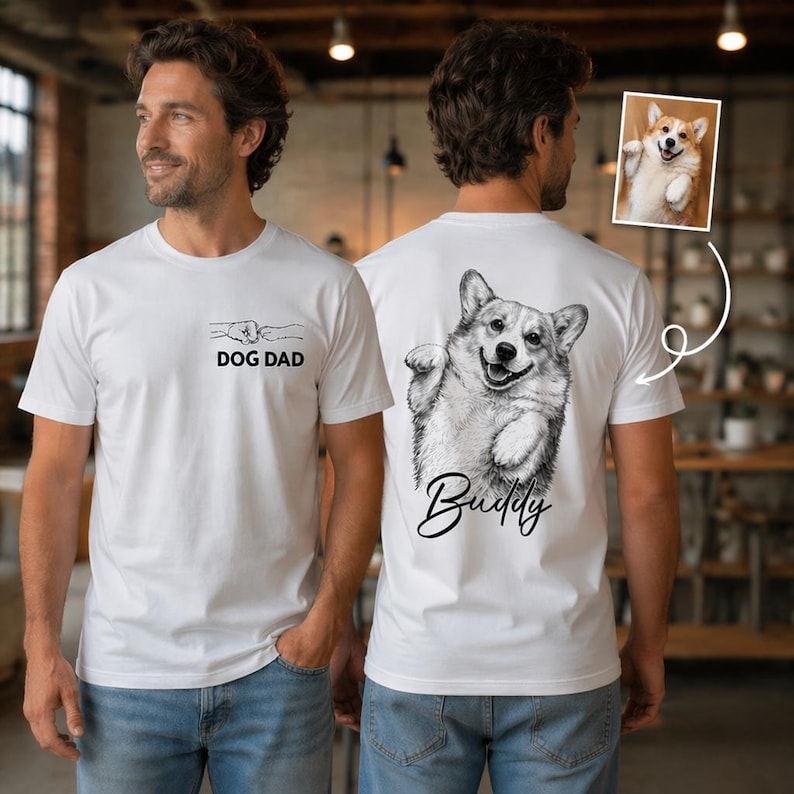 Pode incluir: Uma t-shirt branca com um gr&aacute;fico frontal de um punho e o texto DOG DAD. As costas exibem um grande esbo&ccedil;o a preto e branco de um Corgi com o nome Buddy escrito por baixo, correspondendo a uma pequena foto do mesmo c&atilde;o.