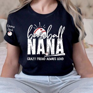 Peut inclure: T-shirt noir avec l'inscription blanche "Baseball NANA", accompagn&eacute;e d'un graphisme de baseball et de batte. Le texte "Crazy Proud Always Loud" est en dessous. Un petit graphisme circulaire avec le texte "Emma Jack" est sur la manche gauche.