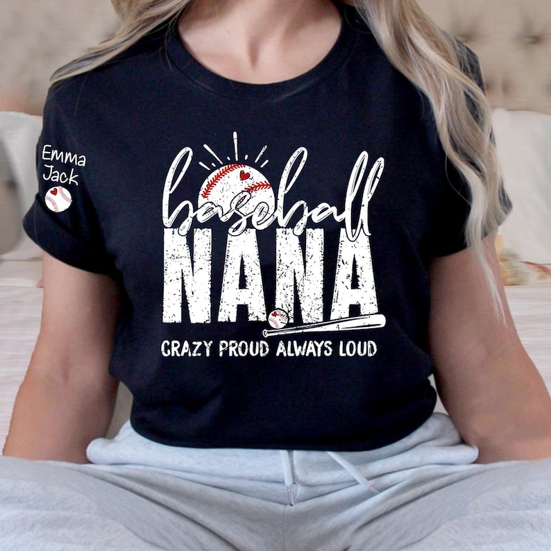 Peut inclure: T-shirt noir avec l'inscription blanche "Baseball NANA", accompagn&eacute;e d'un graphisme de baseball et de batte. Le texte "Crazy Proud Always Loud" est en dessous. Un petit graphisme circulaire avec le texte "Emma Jack" est sur la manche gauche.