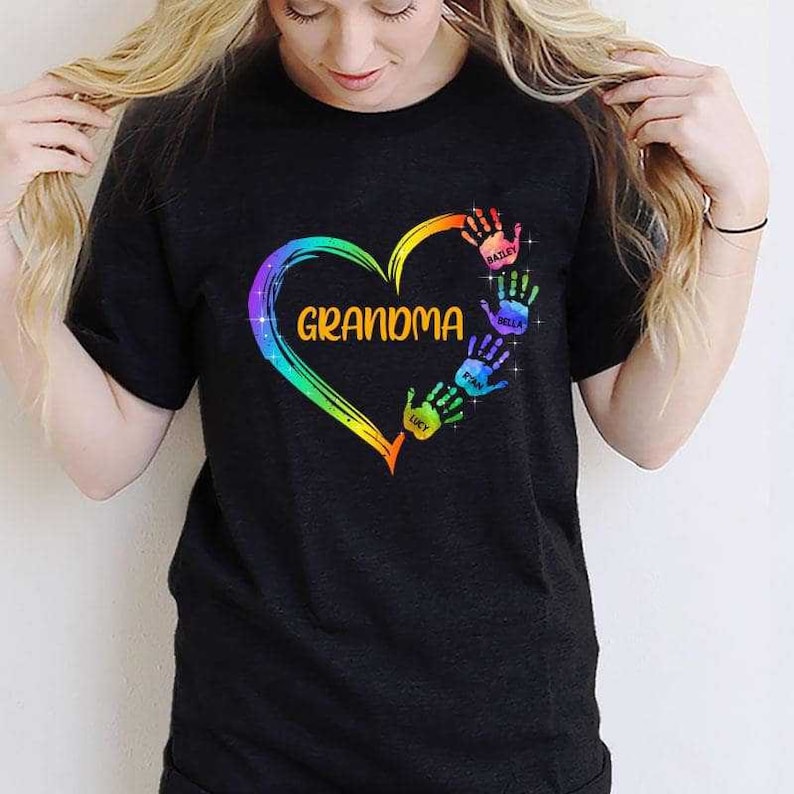Pu&ograve; includere: Maglietta nera con un design a forma di cuore arcobaleno e la parola "Nonna" all'interno del cuore. Il cuore &egrave; circondato da impronte di mani colorate con i nomi scritti sotto ogni impronta: Bailey, Bella, Finn, Lucy.