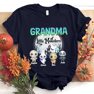K&ouml;nnte beinhalten: Ein marineblaues T-Shirt mit dem Text "Grandma of Little Monsters" in Gr&uuml;n und Wei&szlig;. Das Shirt zeigt vier Cartoon-Monster mit den Namen Sophia, James, Max und Josh.