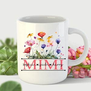 May include: White ceramic mug with a watercolor floral design featuring colorful flowers and green leaves. The text "MIMI" is printed in black with the names "sophia", "jack", and "harry" printed in pink below the floral design.