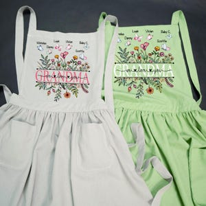 May include: Two floral print aprons with the word "Grandma" and the phrase "We love you" in pink lettering. The aprons have pockets and adjustable straps. The aprons are personalized with names and butterflies.