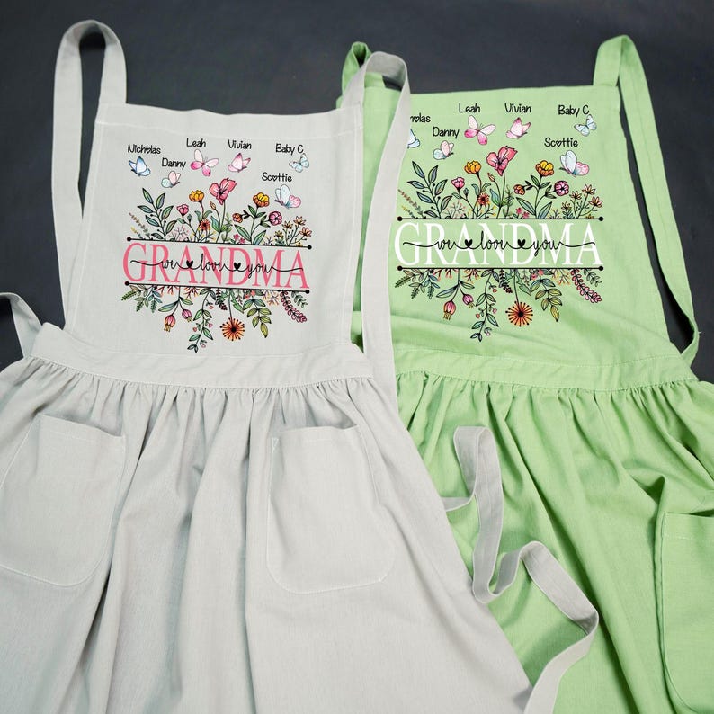 May include: Two floral print aprons with the word "Grandma" and the phrase "We love you" in pink lettering. The aprons have pockets and adjustable straps. The aprons are personalized with names and butterflies.
