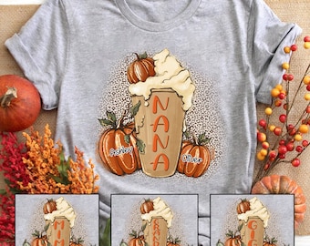 Puede incluir: Una camiseta gris con un diseño de otoño que presenta una taza de café con crema batida y calabazas. El texto "NANA" está escrito en la taza. Las calabazas están etiquetadas con los nombres "Ashley" y "Oliver".