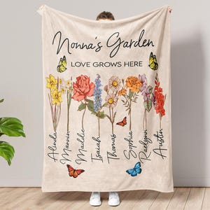 May include: A beige fleece blanket with the text "Nonna's Garden Love Grows Here" and a floral design with butterflies and names written vertically along the stems.