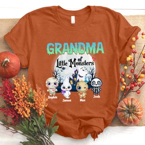 K&ouml;nnte beinhalten: Orangefarbenes T-Shirt mit dem Text "Grandma of Little Monsters" in Gr&uuml;n und Blau. Vier Cartoon-Monster sind abgebildet mit den Namen Sophia, James, Max und Josh.