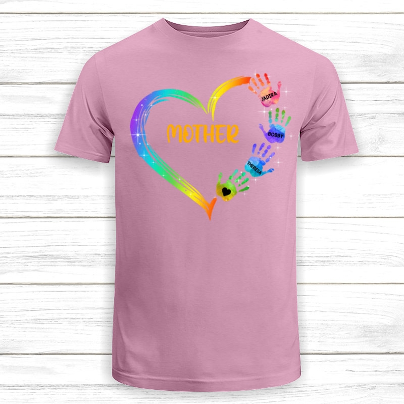 Pu&ograve; includere: Maglietta rosa con un design a forma di cuore arcobaleno e impronte di mani. Le impronte di mani hanno i nomi scritti su di esse: Jaidra, Bobby e Theresa. Il cuore ha la parola "MAMMA" scritta al suo interno.
