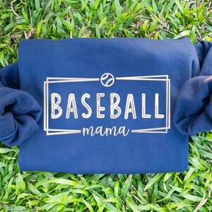 May include: Navy blue sweatshirt with a white embroidered baseball logo and the text "baseball mama".