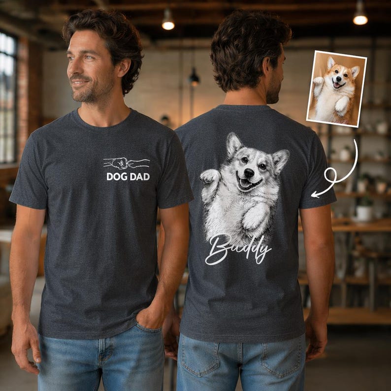 Pode incluir: Uma t-shirt cinzenta escura mesclada com um gr&aacute;fico branco no peito mostrando um toque de punhos entre uma m&atilde;o humana e uma pata de c&atilde;o com o texto DOG DAD. As costas exibem uma grande ilustra&ccedil;&atilde;o a preto e branco de um Corgi com o nome Buddy.