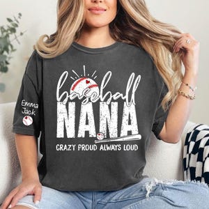 Peut inclure: T-shirt gris fonc&eacute; avec l'inscription blanche "baseball NANA" et un graphisme de baseball. Le texte "CRAZY PROUD ALWAYS LOUD" est en dessous. La manche porte le nom "Emma Jack" et un graphisme de baseball.