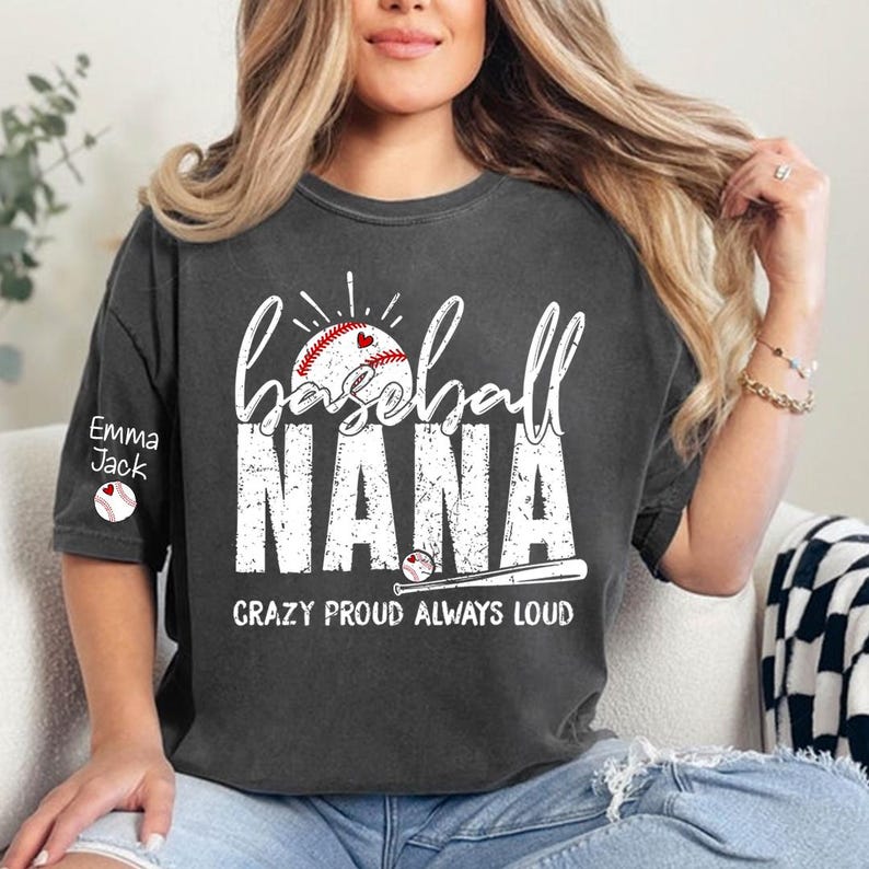 Peut inclure: T-shirt gris fonc&eacute; avec l'inscription blanche "baseball NANA" et un graphisme de baseball. Le texte "CRAZY PROUD ALWAYS LOUD" est en dessous. La manche porte le nom "Emma Jack" et un graphisme de baseball.
