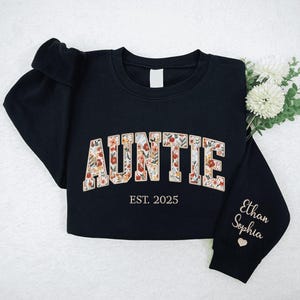 May include: Black sweatshirt with the text "AUNTIE EST. 2025" in floral lettering. The left sleeve has the names "Ethan Sophia" embroidered in gold.