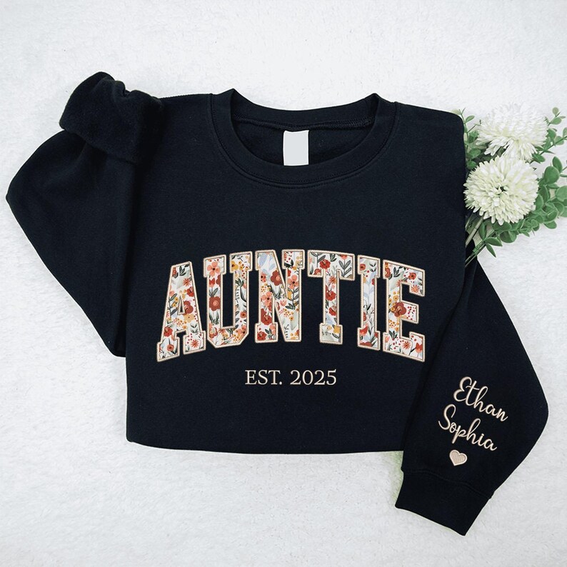 May include: Black sweatshirt with the text "AUNTIE EST. 2025" in floral lettering. The left sleeve has the names "Ethan Sophia" embroidered in gold.