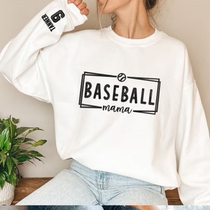 May include: White sweatshirt with a black graphic that says "BASEBALL mama" with a baseball icon. The left sleeve has a black number "6" and the word "TAMMER" above it.