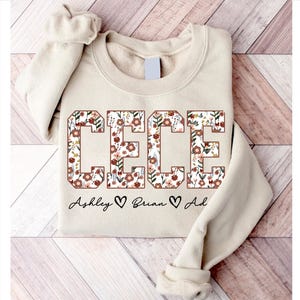 May include: A beige sweatshirt with the name "CEECE" in large, block letters. The letters are filled with a floral pattern in shades of pink, red, and brown. The text "Ashley ♥ Brian ♥ Ad" is written below the name.