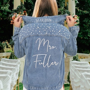 May include: A light blue denim jacket with white pearl embellishments on the back. The text "Mrs. Fuller" and the date "12.12.2024" are embroidered on the back of the jacket.
