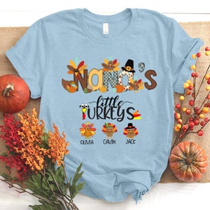May include: Light blue t-shirt with a Thanksgiving theme. The shirt features the text "Nana's little turkeys" with a turkey illustration for each of the names Olivia, Gavin, and Jack.