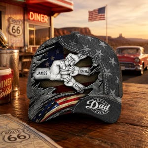 May include: A gray denim baseball cap with a distressed American flag design. The cap features a graphic of four hands clasped together, with the names "James", "Jacob", "Emma", and "Liam" printed on them. The words "Best Dad Ever" are also on the cap.