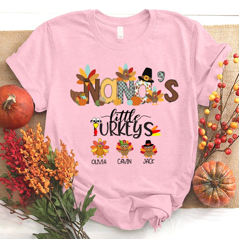 May include: Pink t-shirt with a Thanksgiving theme. The shirt features the text "Nana's Little Turkeys" with a turkey illustration for each name: Olivia,  Gavin, and Jack.