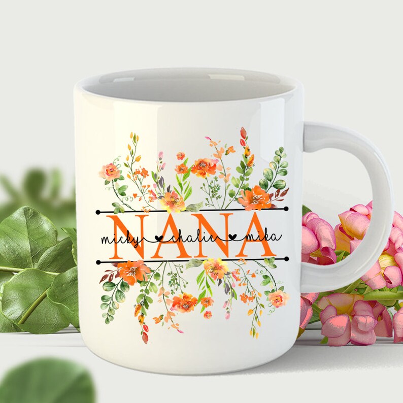 May include: White ceramic mug with a floral design in shades of orange and green. The word "NANA" is printed in orange with the names "micky", "chalin", and "mika" printed below in black.