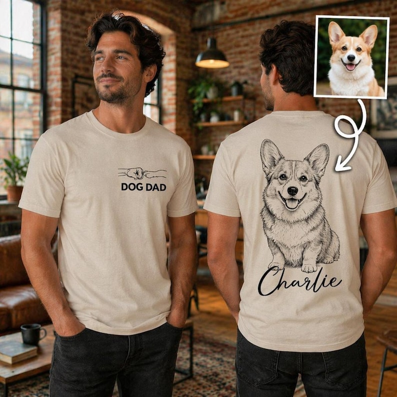 Pode incluir: Uma t-shirt bege com um pequeno gr&aacute;fico no peito de um punho humano a bater com uma pata de c&atilde;o e o texto DOG DAD. A parte de tr&aacute;s da t-shirt apresenta uma grande ilustra&ccedil;&atilde;o de linhas de um c&atilde;o Corgi com o nome Charlie escrito por baixo.